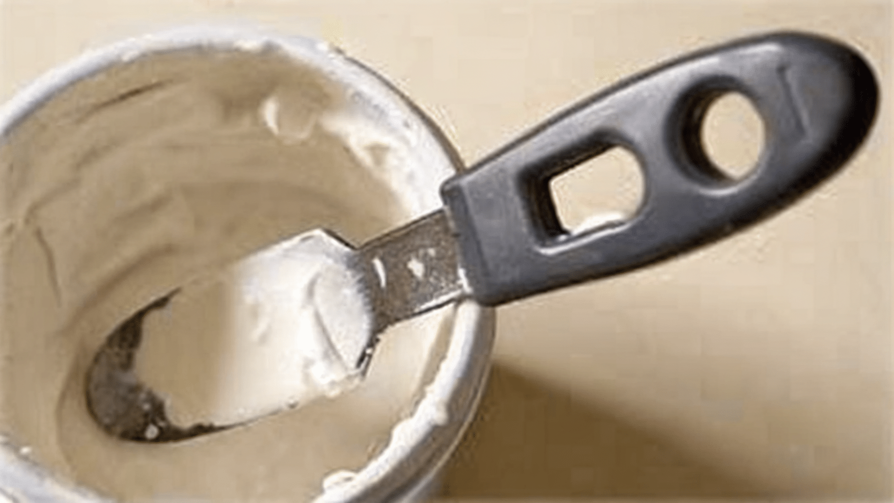 Open container of drywall spackle with a black-handled putty knife resting across the top, ready for use.